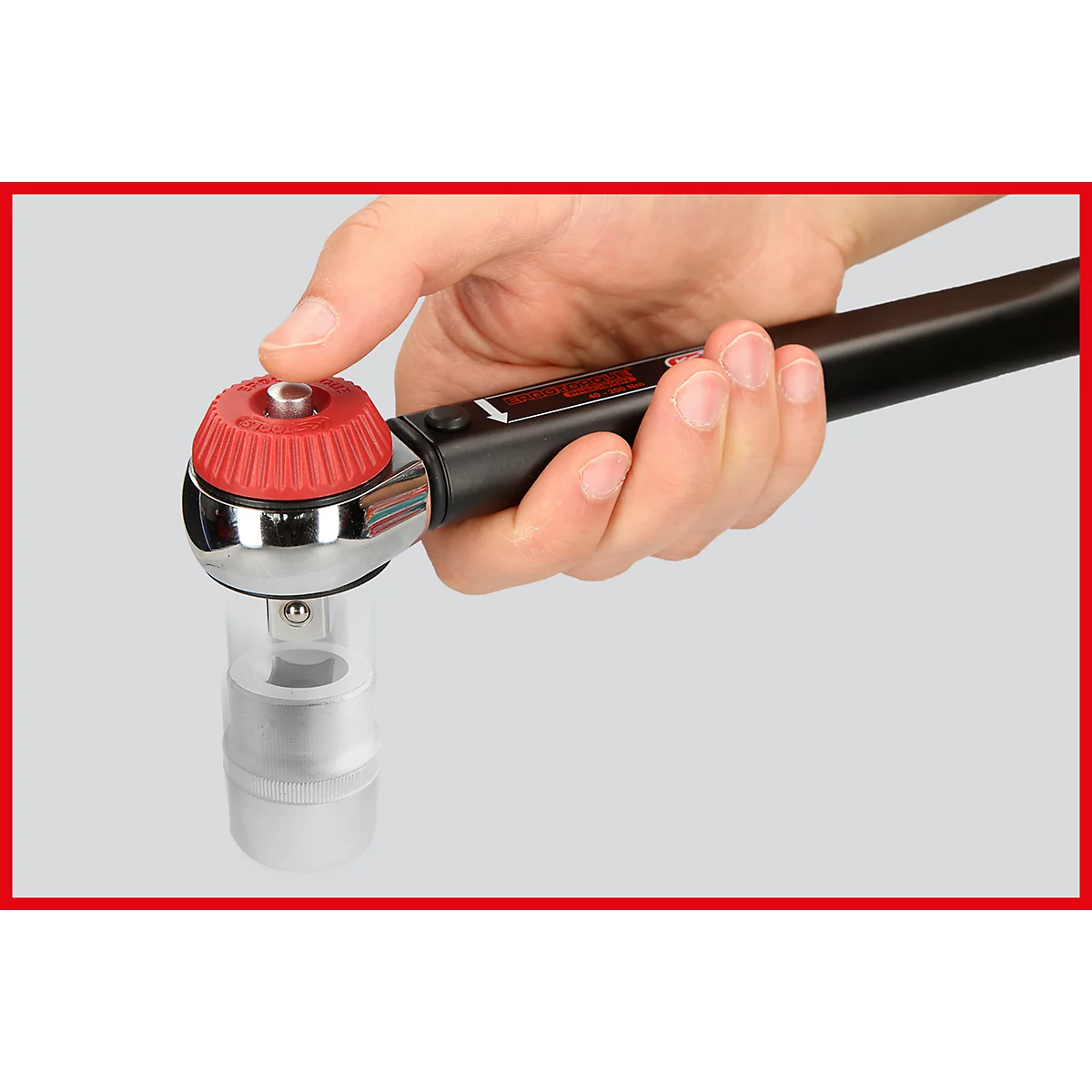 Hand hält einen Drehmomentschlüssel. Der Knopf ist rot, der Rest schwarz und silber.